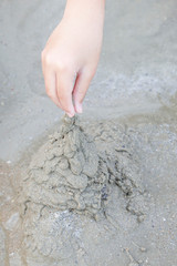 The boy's hand plays a sand pile on the beach.