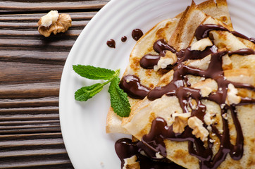 French crepes with chocolate sauce and walnuts in ceramic dish on wooden kitchen table