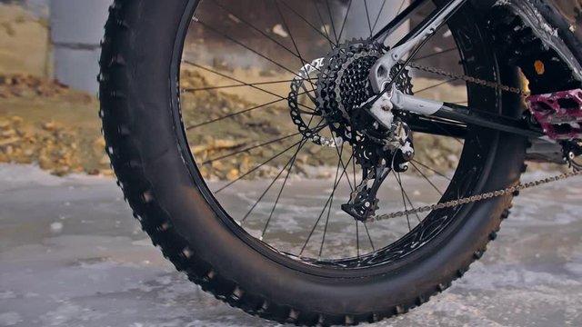 Professional extreme sportsman biker riding fat bike in outdoors. Close-up view of rear wheel. Cyclist ride in winter forest. Man on mountain bicycle with big tire. Snow fly into the lens camera.