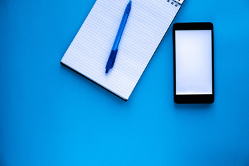 Black phone with a white screen is next to the open, diary and pen on a blue background
