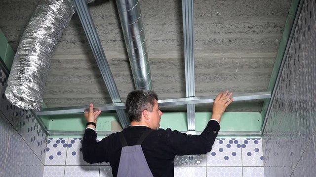 Man fasten ceiling profiles in new flat room