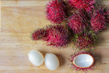 Obraz na płótnie Canvas a bunch of thai exotic fruit rambutan with the whole and clipping ones lying on wooden table with copy spase