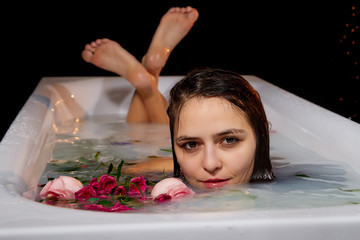 Young pretty brunette woman in bath with white water and flowers in a dark room