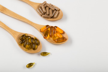 Fish oil capsules in a wooden spoon on white background, omega 3 and vitamin B,C,D healthy diet...