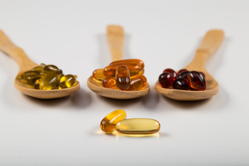 Fish oil capsules in a wooden spoon on white background, omega 3 and vitamin B,C,D healthy diet...