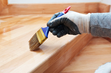 Painter paints a varnish wooden board by brush