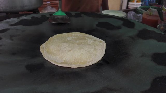 Slow-motion of hands cooking making flipping traditional Indian flat bread, Parotta or Chapatti, with stuffed eggs on large open heated metal pan on the street side in Delhi, handheld stabilized 4k 