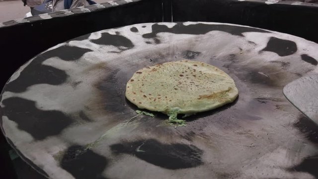 Slow-motion of hands cooking making flipping traditional Indian flat bread, Parotta or Chapatti, with stuffed eggs on large open heated metal pan on the street side in Delhi, handheld stabilized 4k 