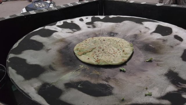 Slow-motion of hands cooking making flipping traditional Indian flat bread, Parotta or Chapatti, with stuffed eggs on large open heated metal pan on the street side in Delhi, handheld stabilized 4k 
