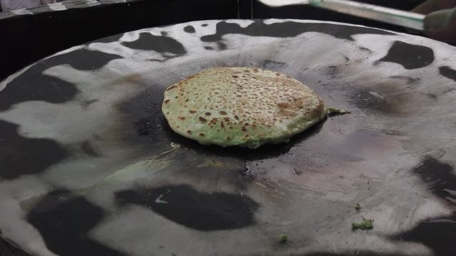 Slow-motion of hands cooking making flipping traditional Indian flat bread, Parotta or Chapatti, with stuffed eggs on large open heated metal pan on the street side in Delhi, handheld stabilized 4k 