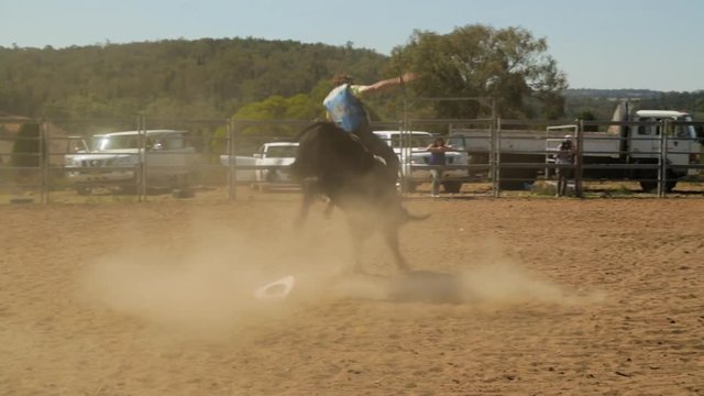 A hand held wide shot of a man riding a bull dangerously on a field as some persons try to calm the bull down
