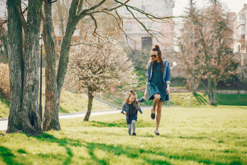 young and stylish mother with long hair and a jeans jacket playing with her little cute daughter in the summer park
