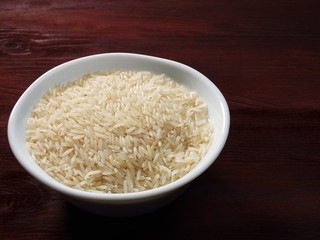 Raw Basmati rice in a white bowl on a brown wooden background