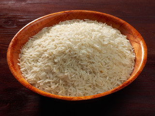 White basmati rice in a bamboo bowl on a brown background