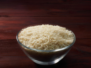 Raw Basmati rice in a glass bowl on a brown wooden background