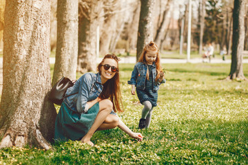 young and stylish mother with long hair and a jeans jacket playing with her little cute daughter in the summer park