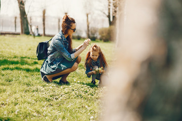 young and stylish mother with long hair and a jeans jacket playing with her little cute daughter in the summer park