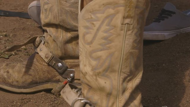 A still close up shot of a pair of cowboy shoes in focus worn by a person with the spur being the most prominent feature