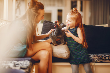 young and stylish mother with long hair and a green dress playing with her little cute daughter and little black rabbit at home