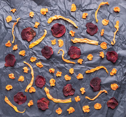 Pattern of vegetable chips on rumpled black wrapping paper. 