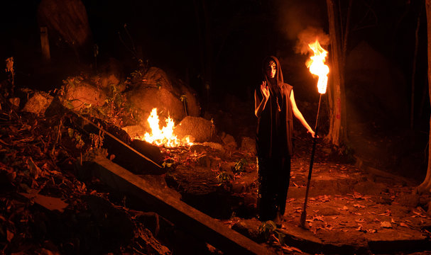 Woman  walking by the dark forest with burning staff