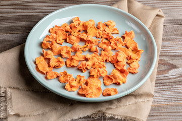 Close-up plate with healthy carrot chips on beige fabric on wooden table.