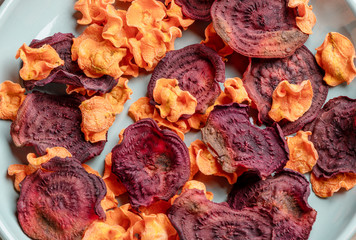 Close-up orange and red chips from carrot and beetroot on turquoise plate.