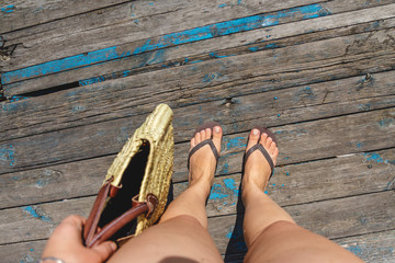 Top view, photo of legs in beach flip-flops and with a straw bag in hand on a wooden old floor....