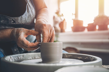 Wrinkled hands wizard on potter wheel makes clay dishes. Place to work