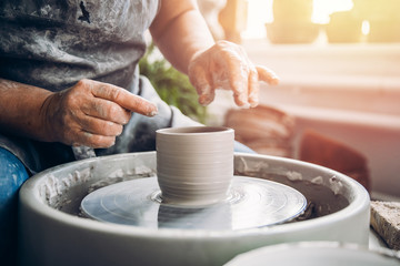 Master holds pot made of clay on potter wheel