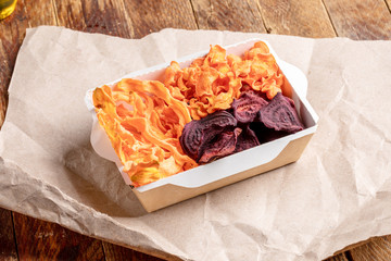Paper box with vegetable chips on wrapping paper on old wooden table.