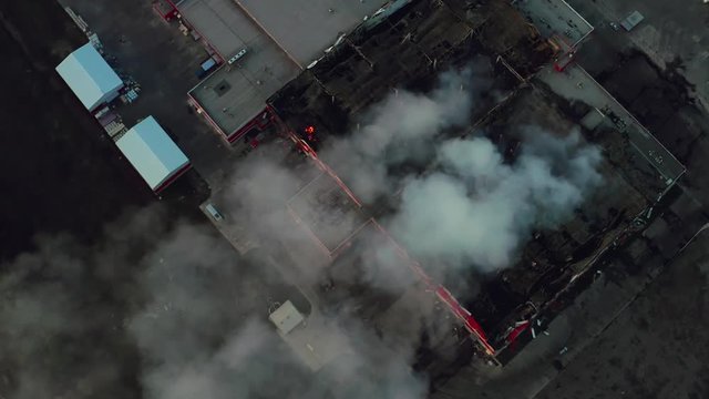 Aerial view of smoke clouds from burnt warehouse building with burned roof, fire disaster accident in cargo logistics storehouse, drone footage