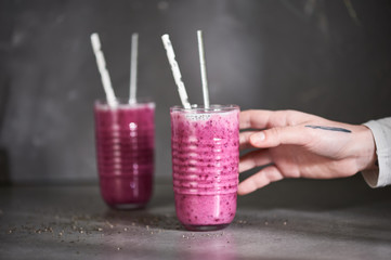 Hand taking glass full of violet smoothie of black currant, yogurt and chia seeds which stands on a gray table