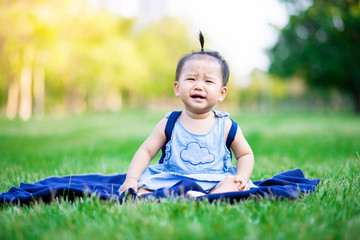 Little adorable baby girl sitting and crying on grass field in the park
