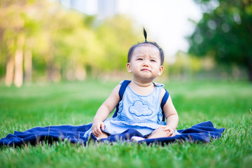 Little adorable baby girl sitting and crying on grass field in the park