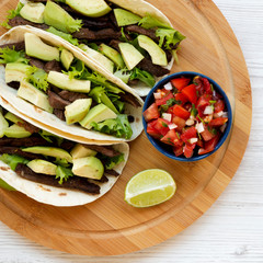 Top view, corn tortillas with grilled beef, avocado, lime and salsa on bamboo board. From above, overhead.