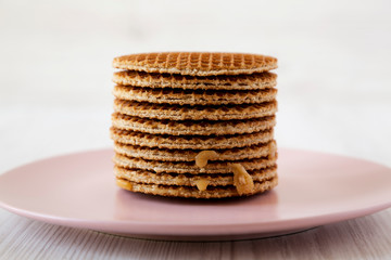 Stack of homemade Dutch stroopwafels with honey-caramel filling on a pink plate, side view. Close-up.