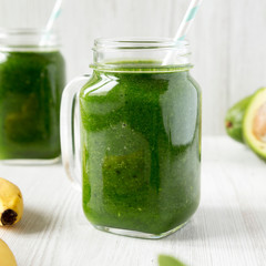 Glass jars full of green smoothie with spinach, avocado and banana over white wooden background, side view. Closeup.