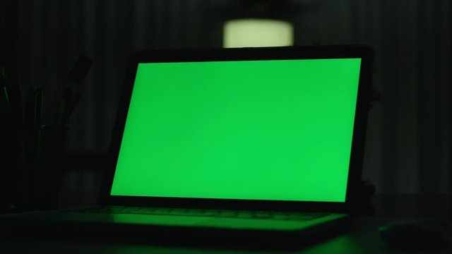 Laptop with green screen. Dark office.  Perfect to put your own image or video.Green screen of technology being used. Chroma Key laptop