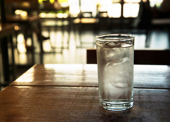 clear glass of cold ice water on brown wood table  with blur bar and restaurant background