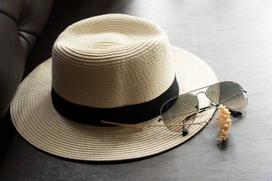 white summer hat with sunglasses with dry flower on black leather sofa
