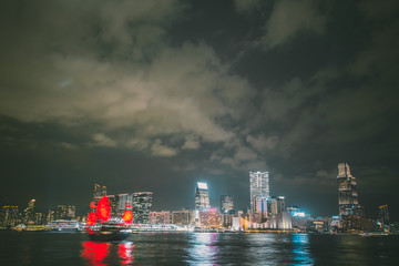 Naklejka premium Panorama of Hong Kong City skyline with tourist sailboat at night.