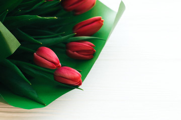 Beautiful stylish tulips bouquet in green paper on white wooden background, top view. Pink tulips on white wood with space for text. Greeting card template. Happy mothers day