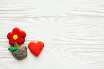Fototapeta premium Plant flower and heart icing cookies on white wood, flat lay with space for text. Delicious sweets. Happy Mothers day. Valentine day