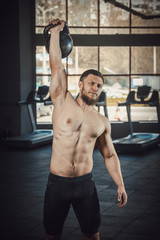Obraz premium athletic young man with beard doing lifting weight at the gym opposite the camera. exercise on the shoulders with weight dumbbells. Guide how to do lifts for shoulders