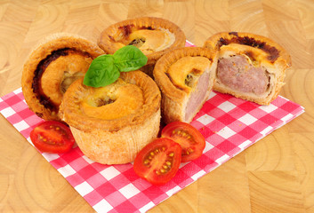 Group of savoury crusty pork pies on a paper gingham pattern napkin with a wood background