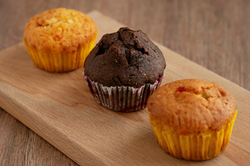 Three muffins on a cutting board. Chocolate muffin and lemon muffins for breakfast. Dessert in the form of muffins on a wooden background close-up.
