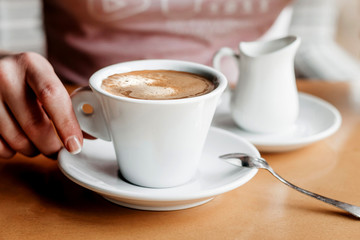 Morning coffee. Closeup of women's hands with coffee cup in a cafe. Female hands holding cups of coffee on a wooden table background in a cafe, vintage color tone