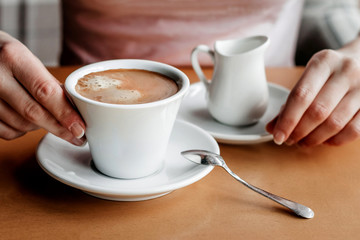 Morning coffee. Closeup of women's hands with coffee cup in a cafe. Female hands holding cups of coffee on a wooden table background in a cafe, vintage color tone