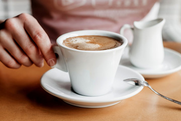 Morning coffee. Closeup of women's hands with coffee cup in a cafe. Female hands holding cups of coffee on a wooden table background in a cafe, vintage color tone